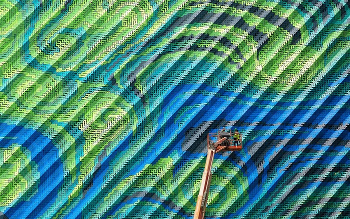 Workers on a lift painting a colorful mural