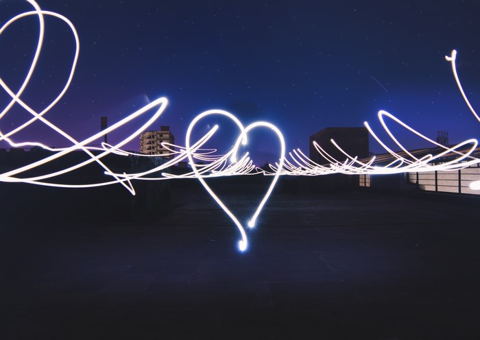 Light painting heart in night sky with stars and buildings