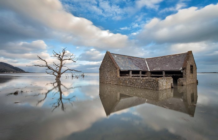 Flooded stone building and dead tree with reflections