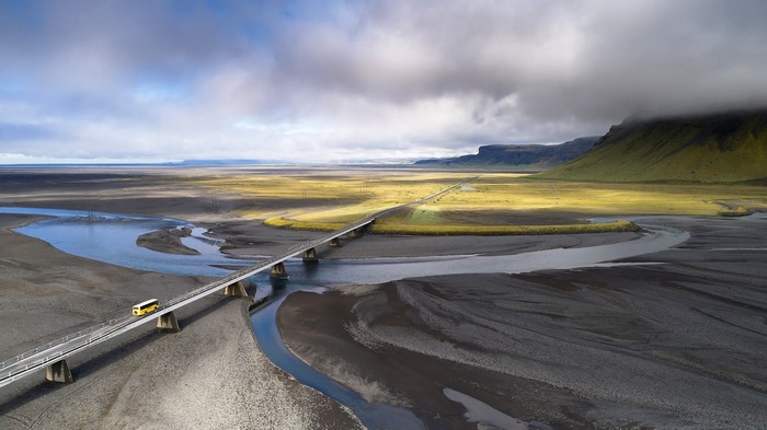Yellow bus crossing a bridge over a river in Iceland