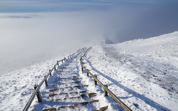 Snowy mountain path with fog and railing