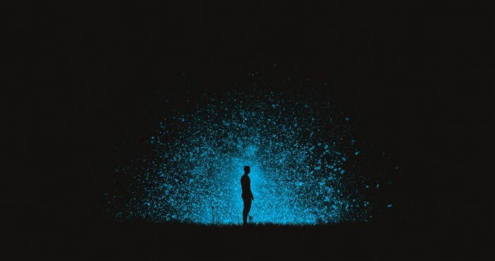 Silhouette of a man with glowing blue particles outdoors at night