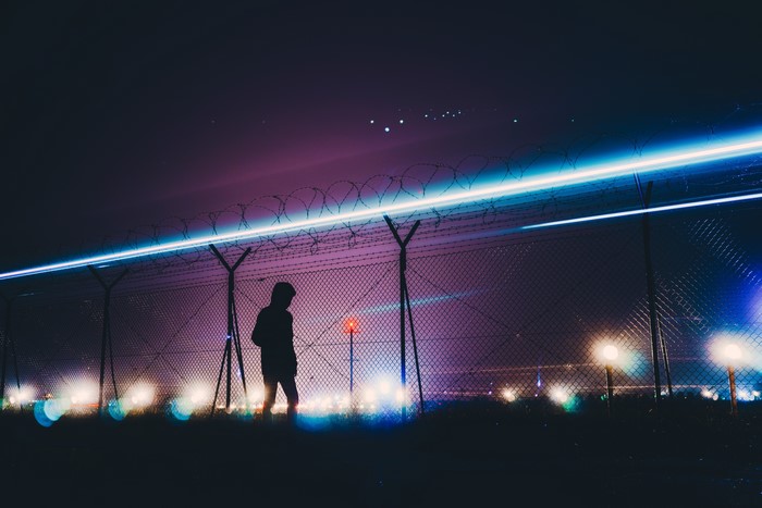 Silhouette by barbed wire fence with light trails at night
