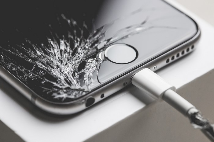 Close-up of a cracked iPhone screen with charging cable