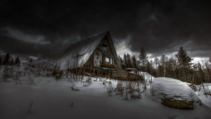 Abandoned A-frame cabin in a snowy forest under dark clouds