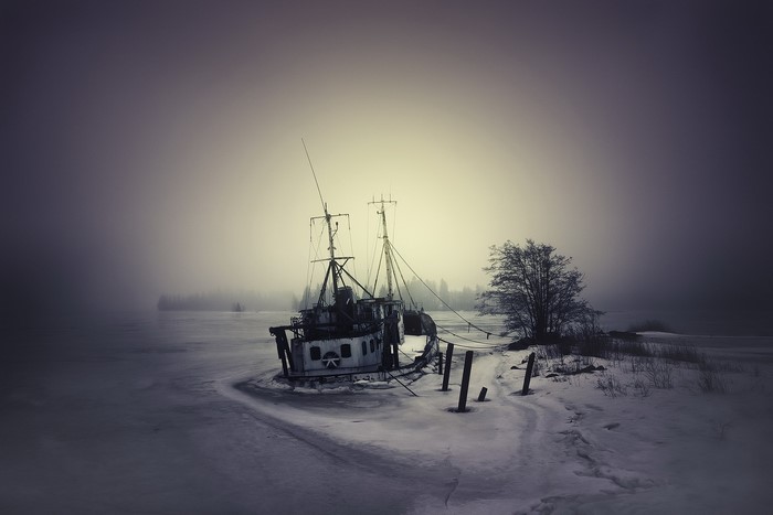 Abandoned boat on a frozen lake in winter mist