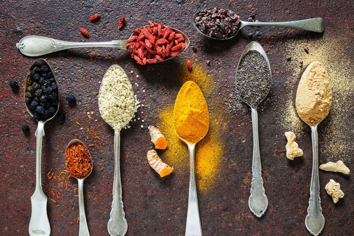 Spoons filled with various spices and seeds on a textured surface