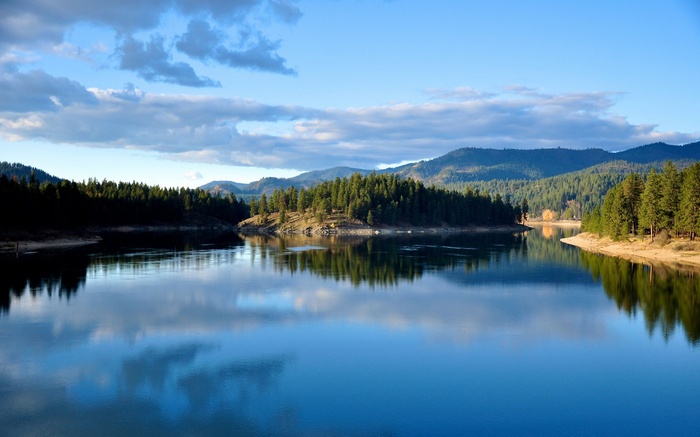 Calm lake reflecting evergreen forest and mountains