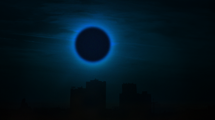 Dark sky with blue eclipse over city skyline