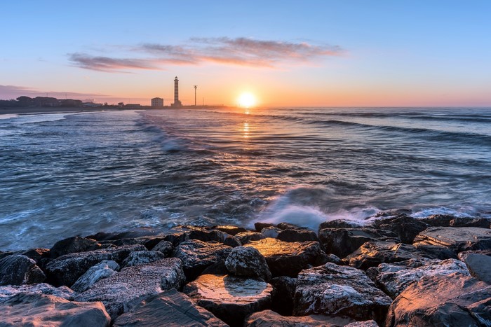 Sunrise over the sea with lighthouse and rocks