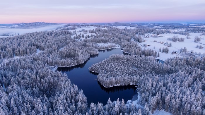 Aerial view of a snow-covered forest surrounding a dark lake