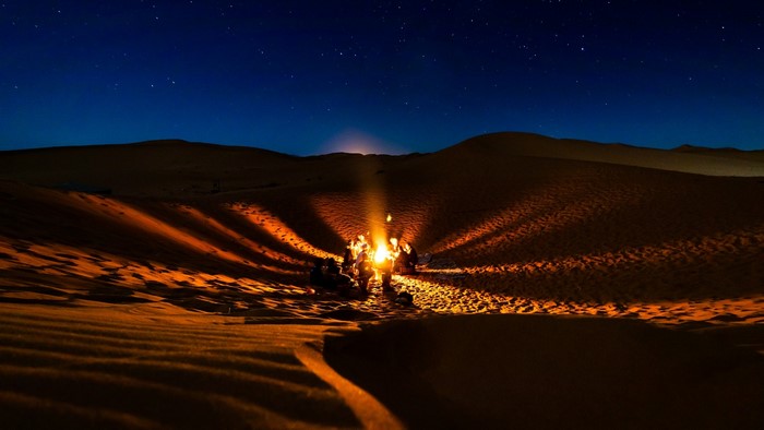 People around a campfire in the desert at night under stars