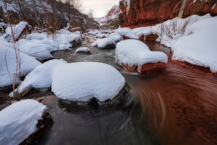 Snowy river flowing through red rocks in winter