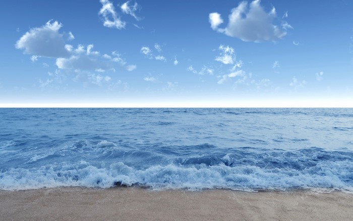 Ocean waves crashing on a sandy beach under a blue sky with clouds