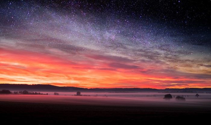 Starry night sky over misty landscape at sunset