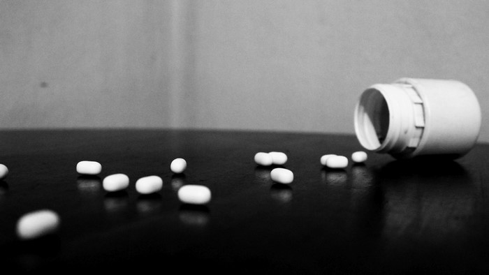 Pills spilled from a bottle on a dark surface