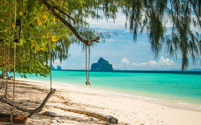 Tropical beach with a swing and island in the distance