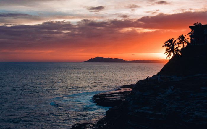 Sunset over the ocean with a silhouette of a cliff and palm trees