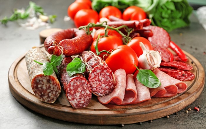 Assortment of cured meats, tomatoes, garlic, and basil on a wooden board