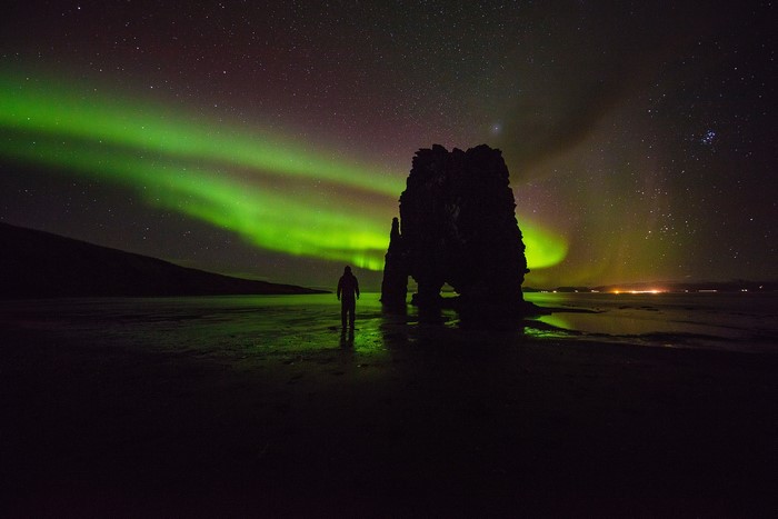 Person watching Aurora Borealis over rock formation