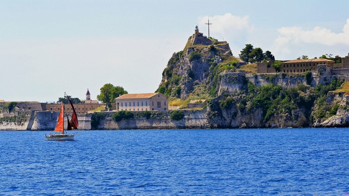 Sailboats near a fortified island with buildings and a lighthouse