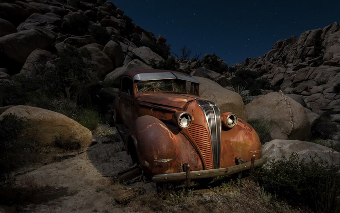 Rusty vintage car in rocky desert landscape at night