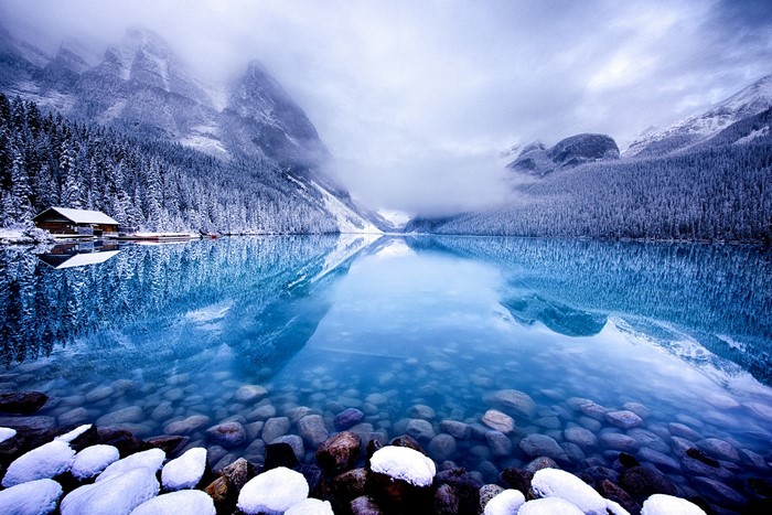 Snowy mountains reflected in a clear blue lake with a cabin