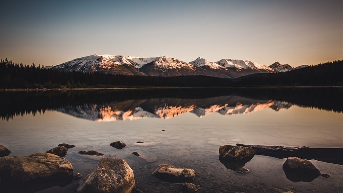 Snowy mountains reflected in a calm lake with rocks in the foreground