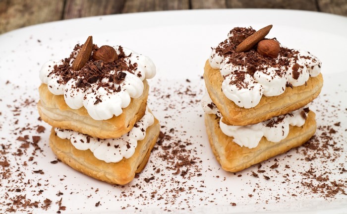 Two stacks of heart-shaped puff pastry desserts with whipped cream and chocolate shavings