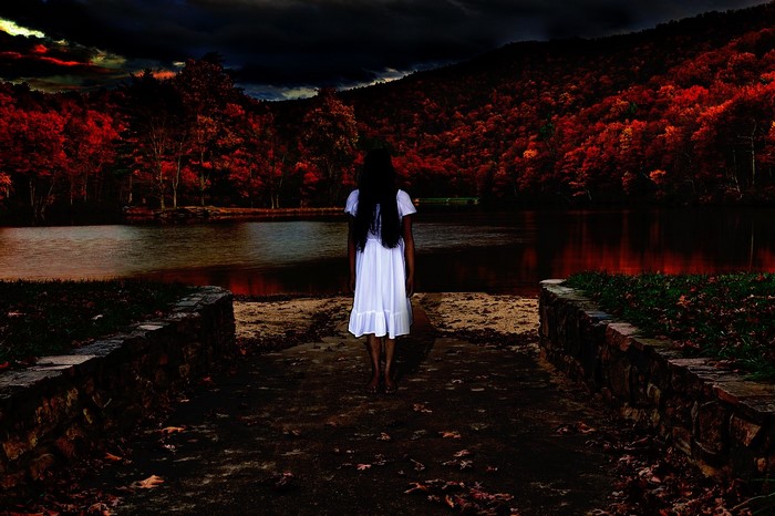 Woman in white dress by a lake with red trees