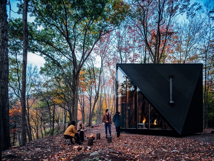 Friends gather around a campfire outside a modern cabin in the woods