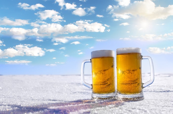 Two mugs of beer in the snow under a cloudy sky