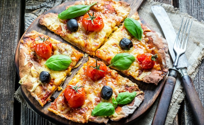 Pizza with tomatoes, olives, and basil on a wooden board