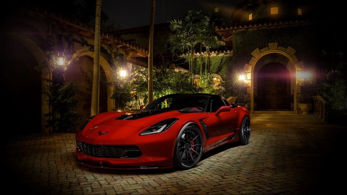 Red Corvette parked in front of a mansion at night
