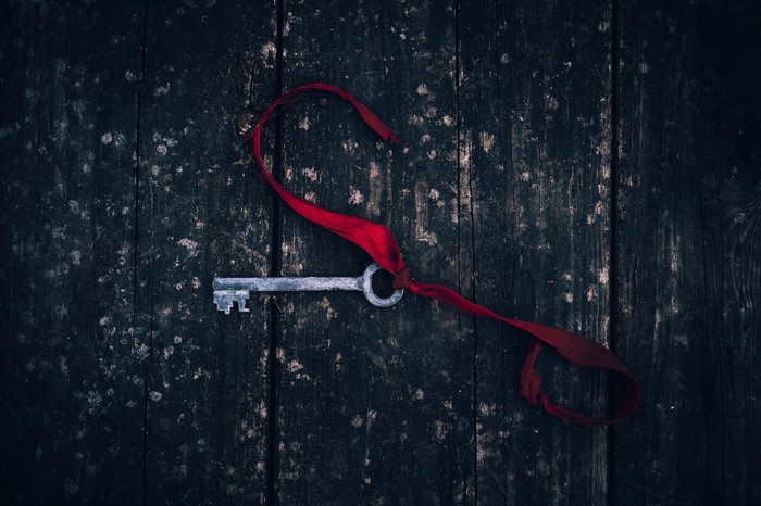 Old key with red ribbon on dark wood