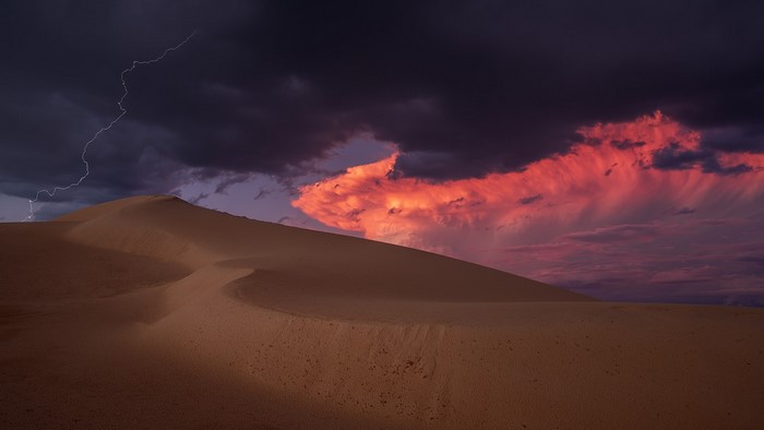 Lightning strikes over desert dunes during a sunset storm