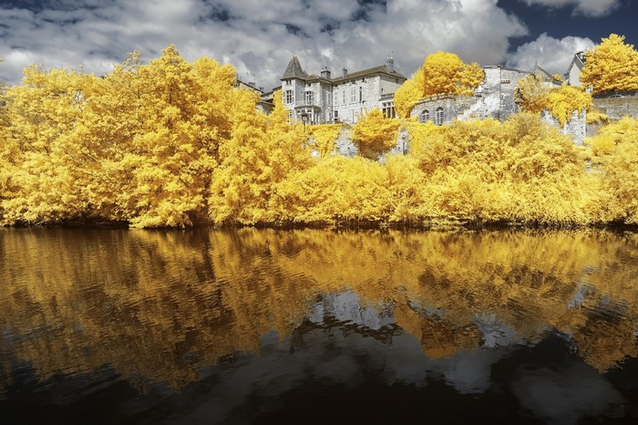 Infrared landscape with yellow trees and a building reflected in water