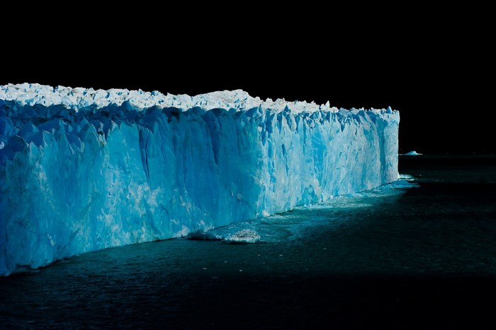 Massive blue glacier wall in dark water