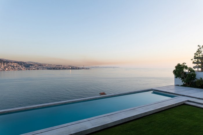 Modern infinity swimming pool overlooking a coastal city at sunset