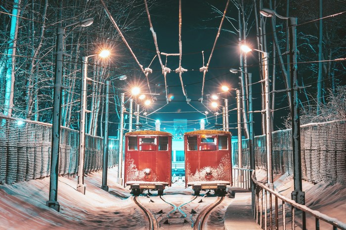 Two red trams on snowy tracks at night in Kaunas