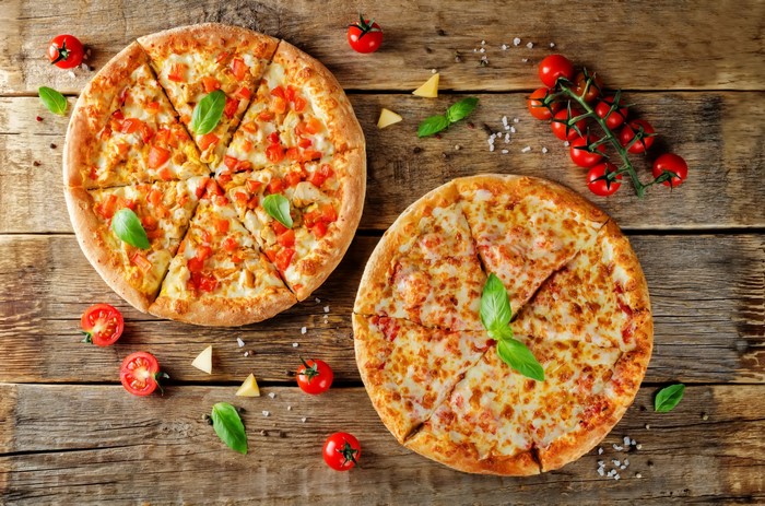 Two pizzas with tomatoes and basil on a wooden surface