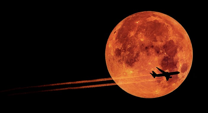 Airplane flying past a blood moon with contrails