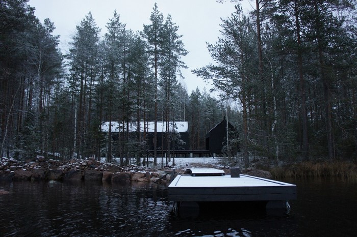 Snowy forest with modern black houses and a dock
