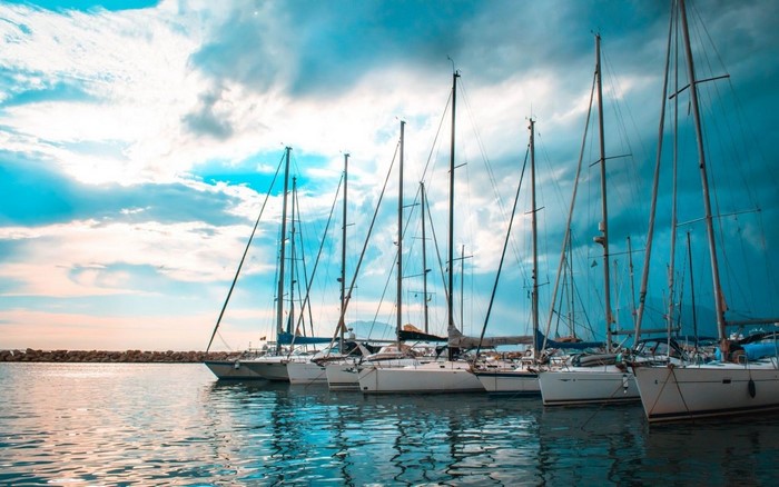 Sailboats docked in a harbor under a cloudy sky
