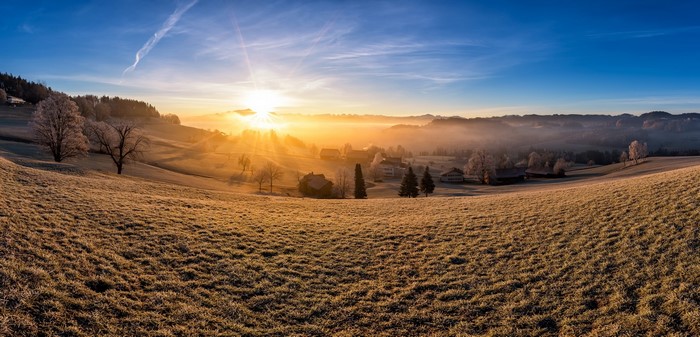 Panoramic sunrise over a misty, frosted landscape with houses