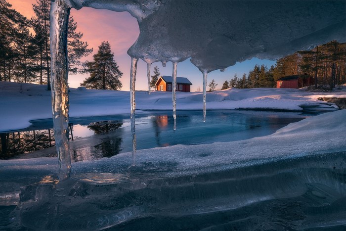 Winter sunset over frozen lake with cabin and icicles