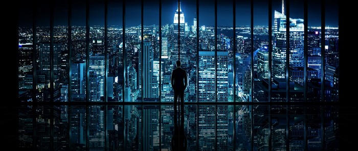 Man looking out window at New York City at night