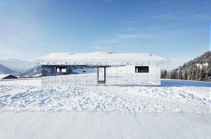 Mirror cabin in snowy landscape with mountains and forest