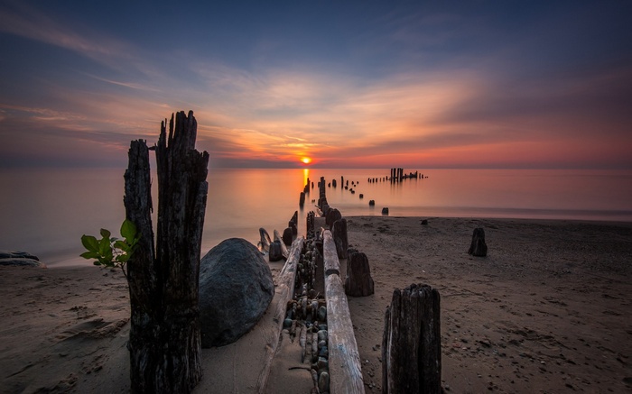 Sunset over a calm ocean with a decaying pier