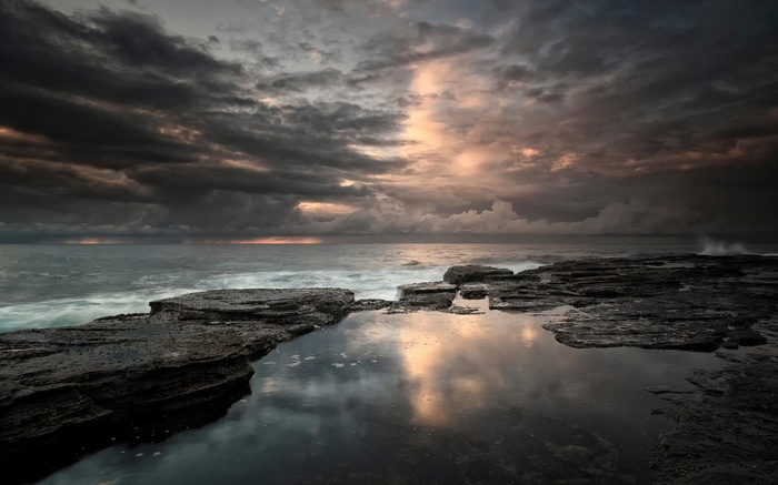 Rocky coastline with stormy clouds and ocean reflection